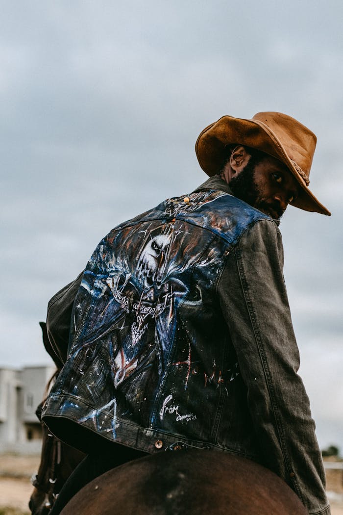 A cool African cowboy in a customized jacket riding his horse.